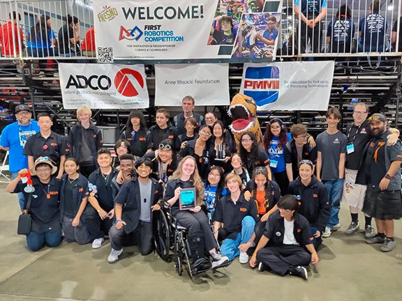 Uni-Rex Robotics team posing in front of sponsorship banners and the FIRST Robotics Competition Welcome banner.
