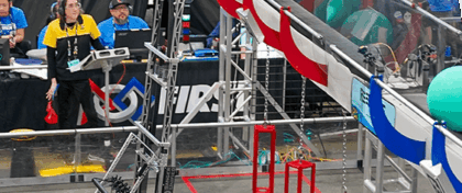 A red FRC robot numbered 5817 extends a mechanism to place a large teal ball into a scoring area during a robotics competition.